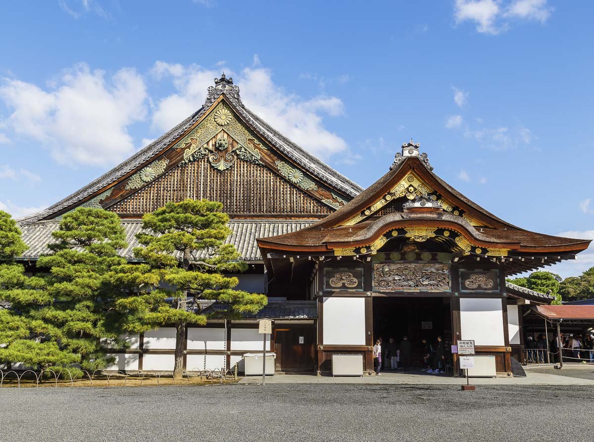 Entrada do Castelo de Nijō com portão ornamentado e edifícios históricos ao fundo.