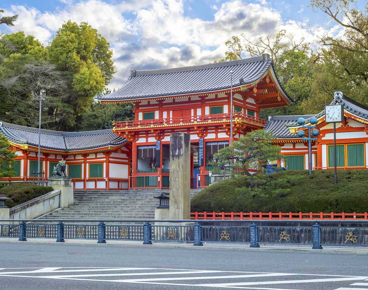 Portão e edifícios do Santuário Yasaka, em Kyoto, com fachada vermelha e branca e escadaria de acesso.
