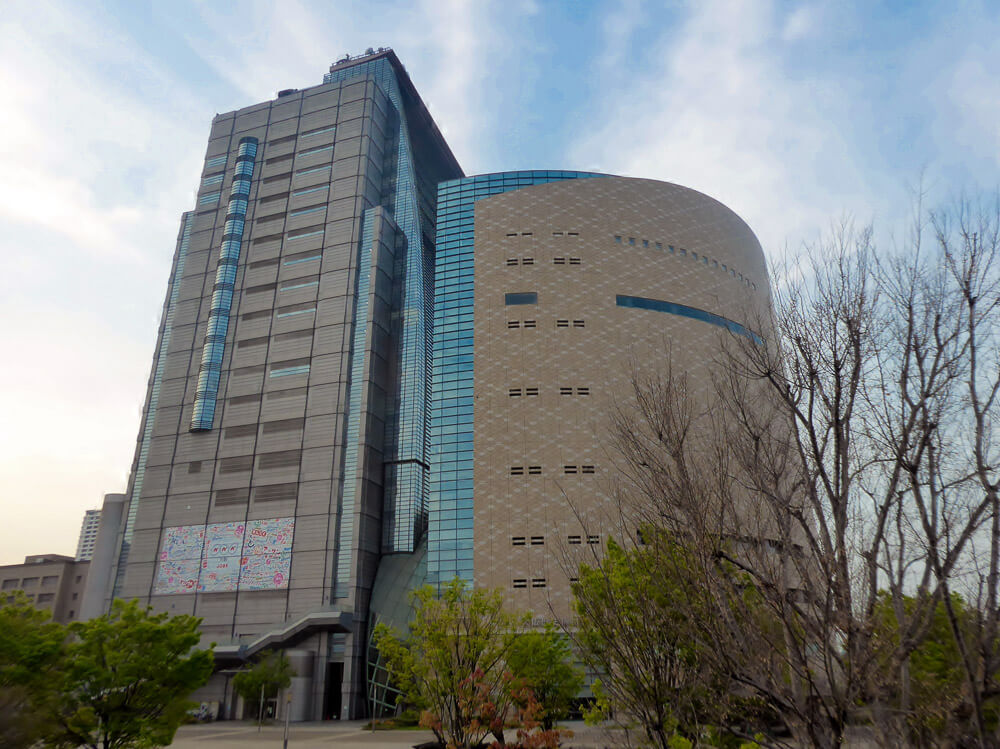 Prédio moderno do Museu de História de Osaka, com fachada curva e torre alta ao lado.
