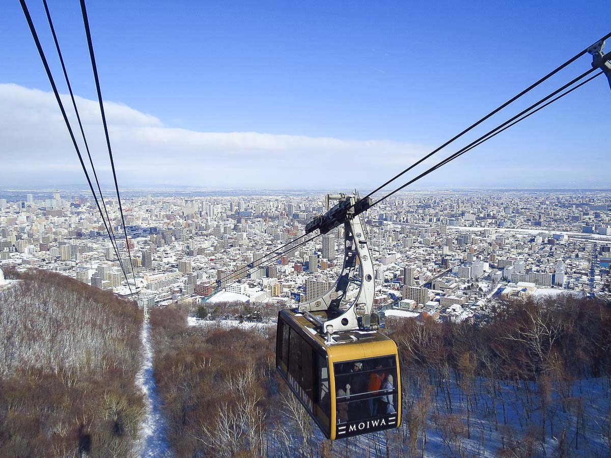Vista panorâmica de Sapporo no inverno, com teleférico do Monte Moiwa e a cidade coberta de neve ao fundo.