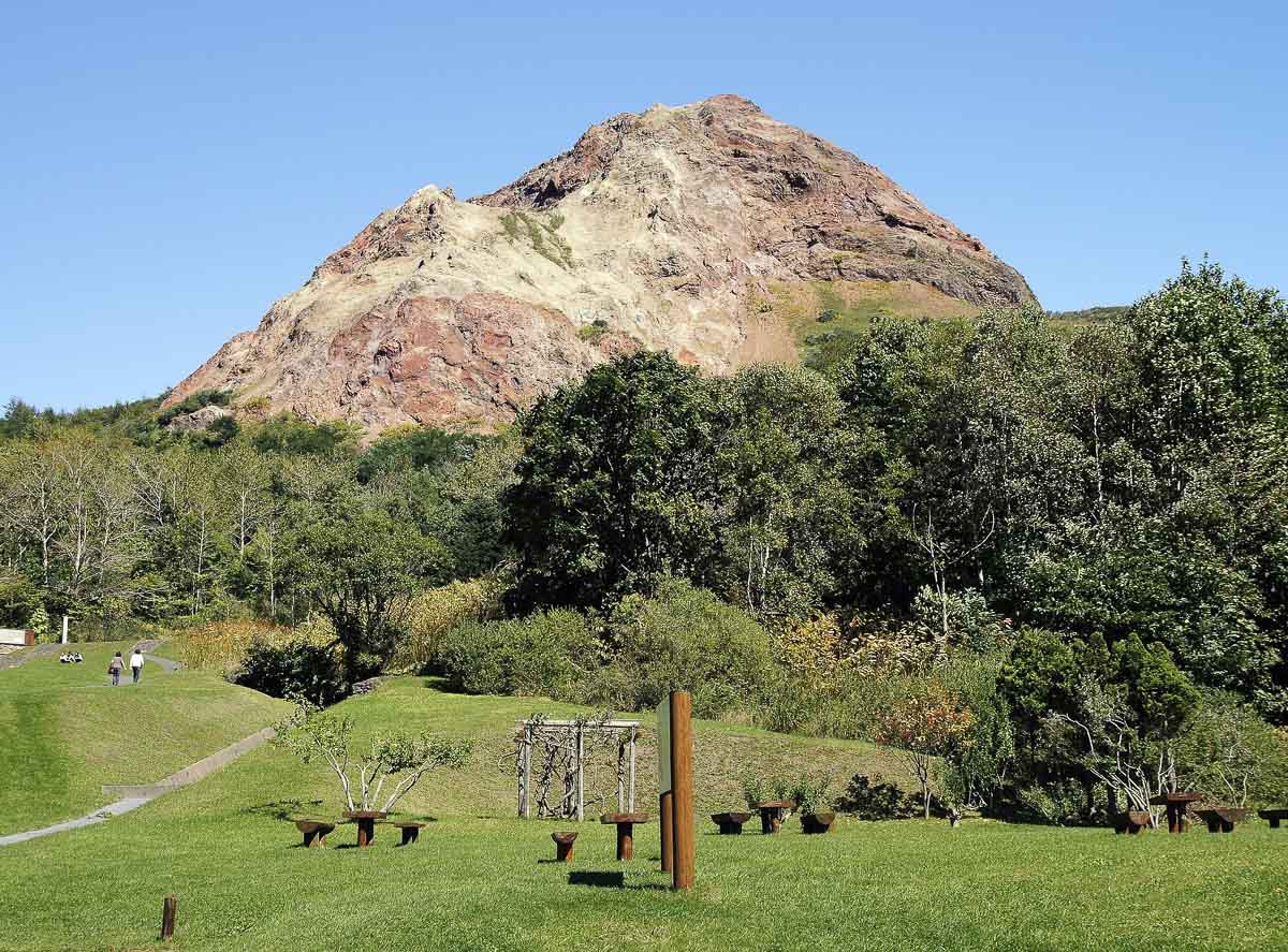 Monte Showa Shinzan, com encosta rochosa, vegetação verde e trilhas ao redor.