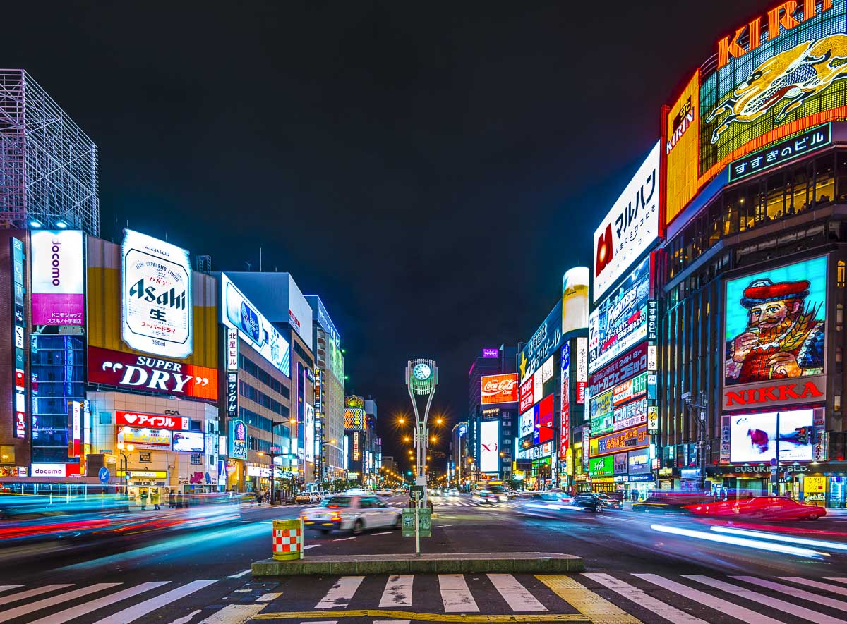 Avenida de Susukino à noite, em Sapporo, com letreiros iluminados e tráfego intenso.