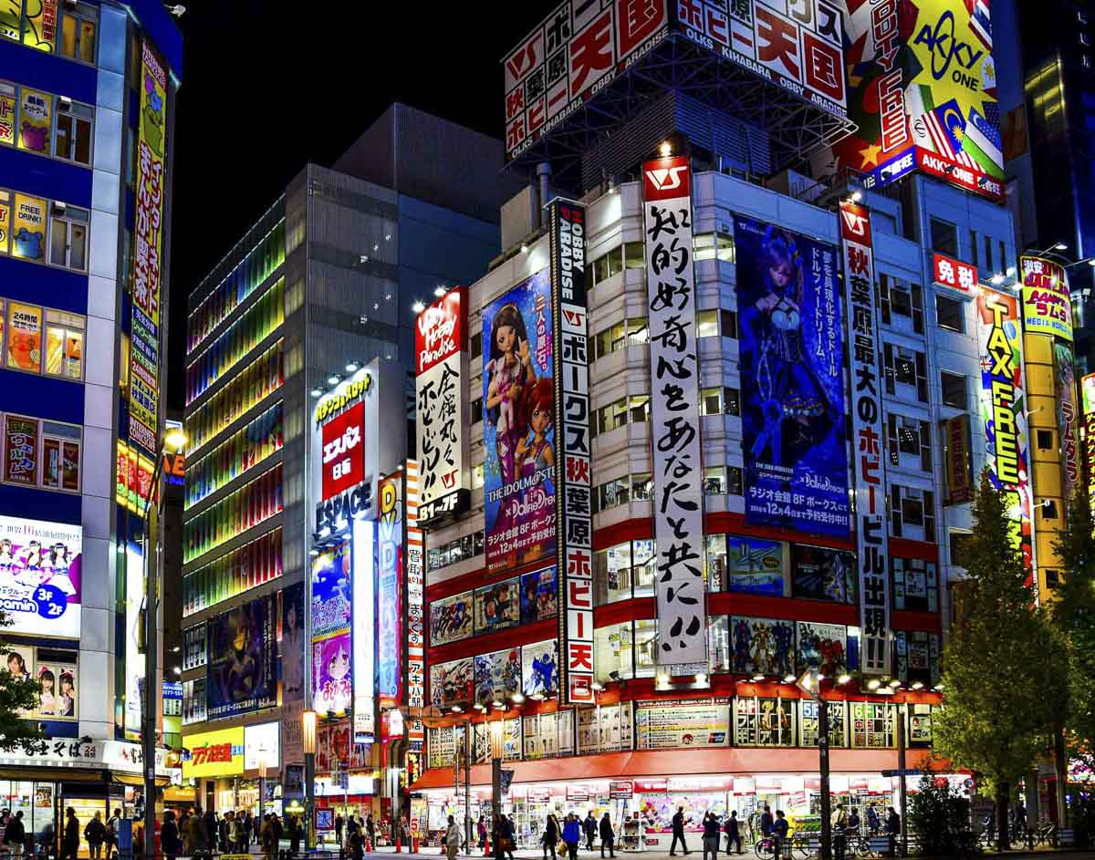 Rua iluminada de Akihabara à noite com prédios cheios de anúncios de anime e eletrônicos