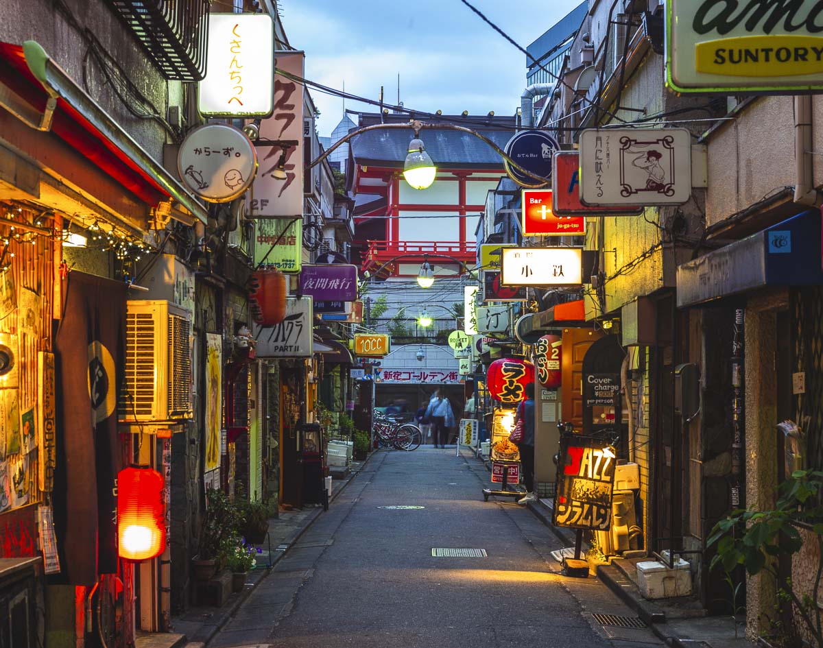 Rua estreita do Golden Gai, em Tokyo, com bares pequenos, lanternas e placas iluminadas