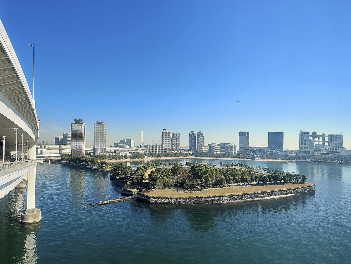 Vista de Odaiba com ilha arborizada, água calma e prédios modernos ao fundo em Tóquio