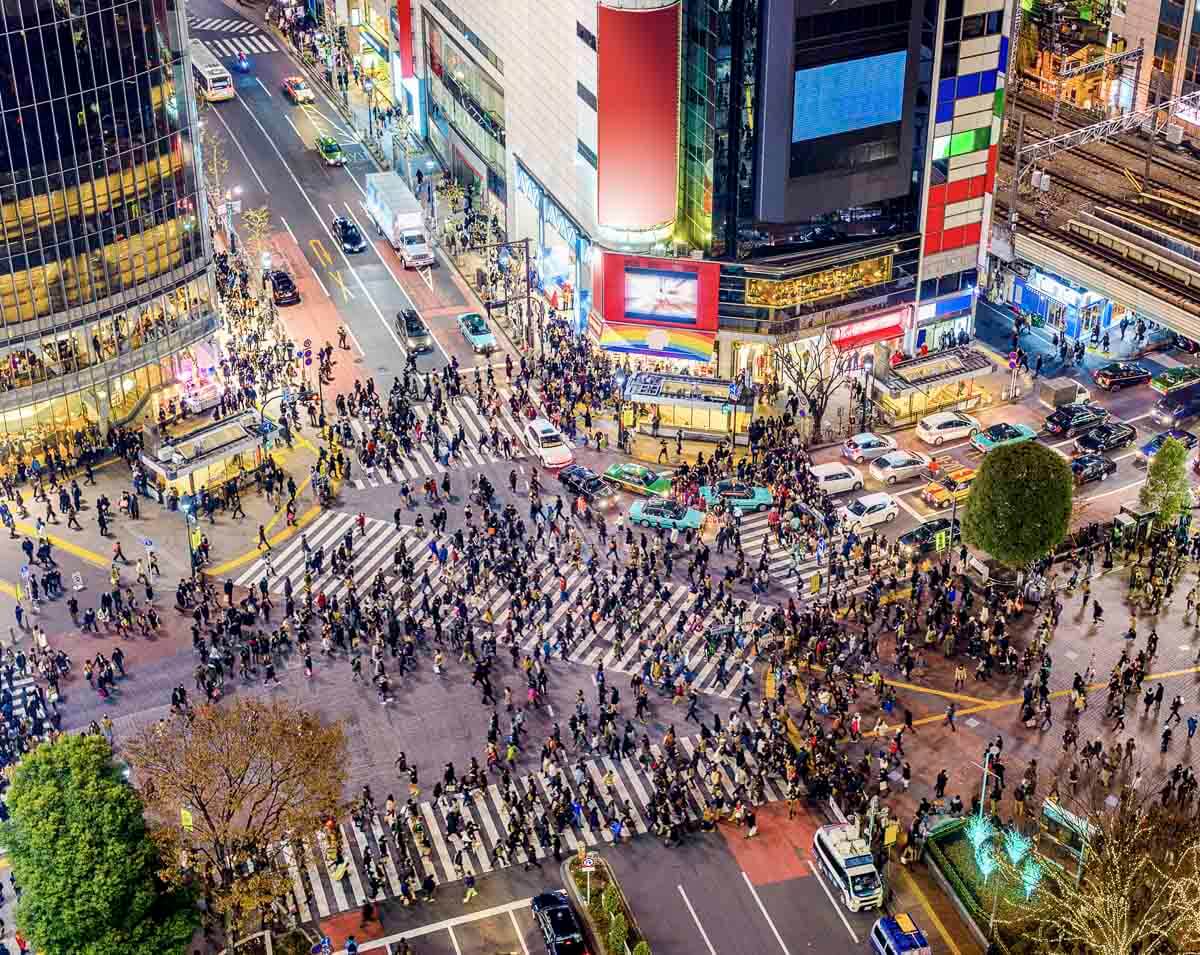 Vista aérea do cruzamento de Shibuya à noite, em Tokyo, com multidão atravessando.