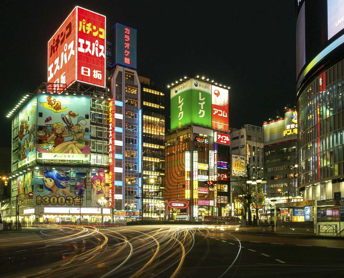 Cruzamento de Shinjuku à noite, em Tokyo, com prédios iluminados e trilhas de luz