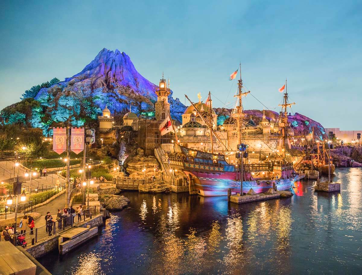Área temática da Tokyo DisneySea ao entardecer, com montanha, navio e iluminação