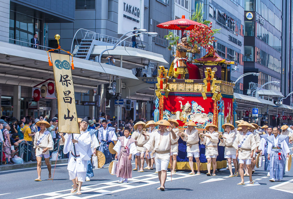 Desfile do Gion Matsuri em Kyoto com participantes em trajes tradicionais carregando um carro alegórico.