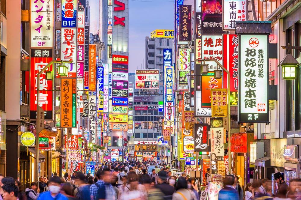 Kabukicho, em Tóquio à noite, com muitas placas luminosas em japonês e grande fluxo de pedestres.