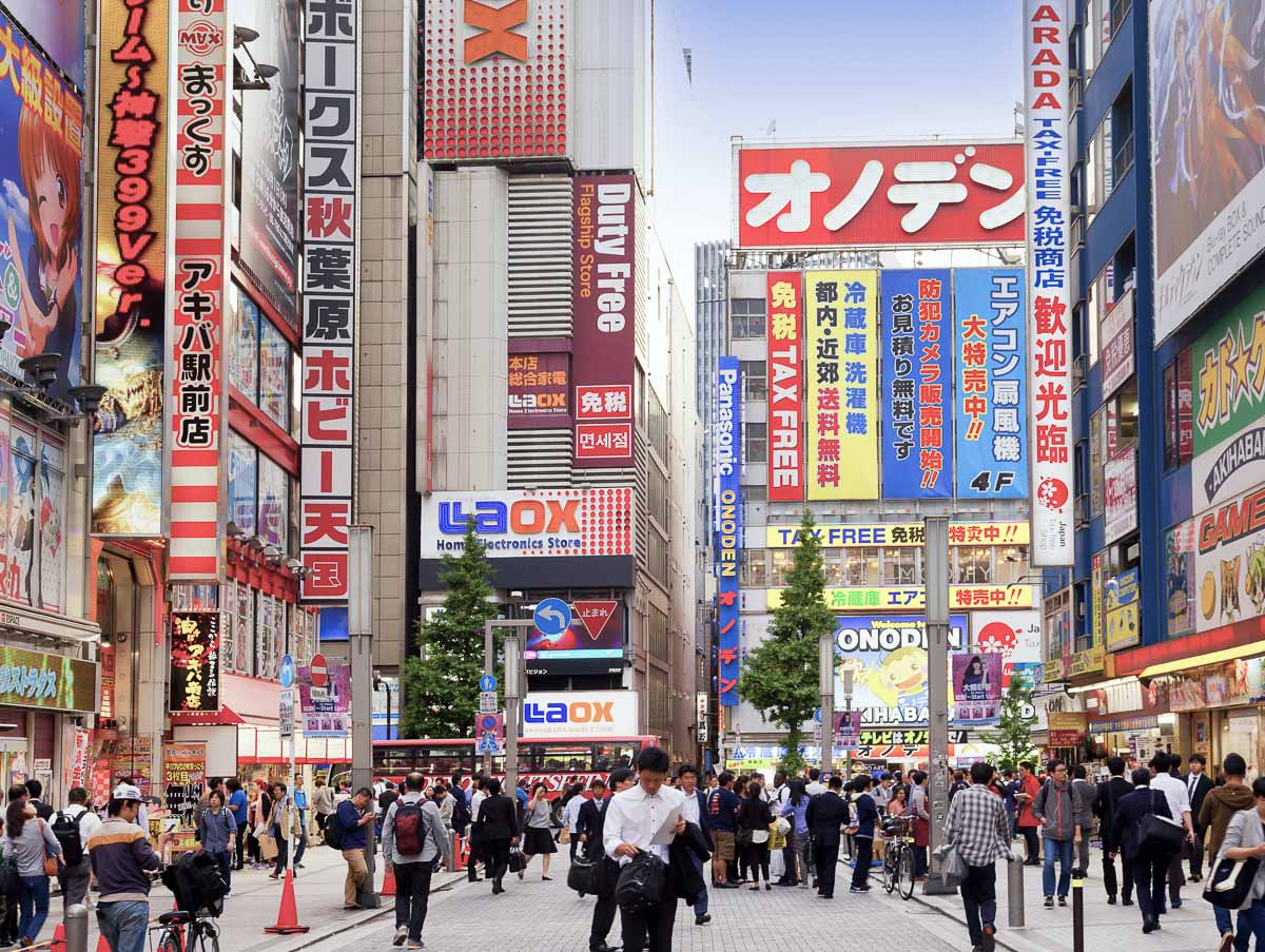 Rua movimentada de Akihabara, em Tokyo, com prédios altos, letreiros coloridos e pedestres