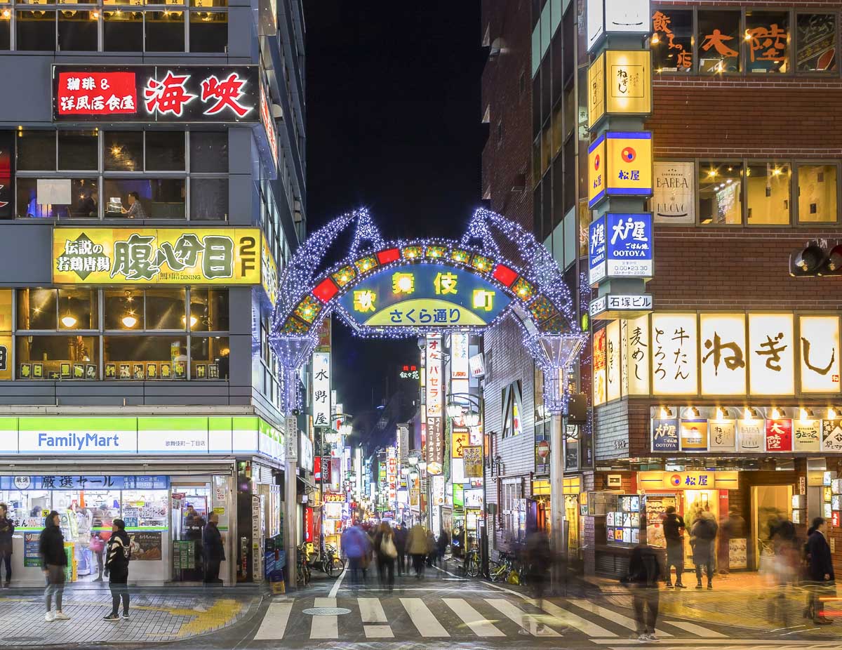 Rua iluminada de Shinjuku à noite, em Tóquio, com bares e letreiros.