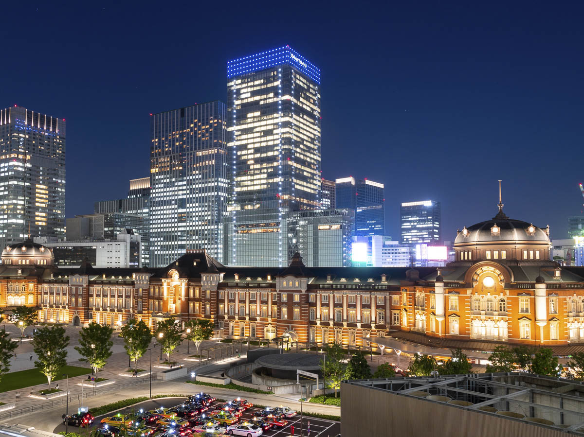 Vista noturna da Estação de Tokyo iluminada com prédios modernos ao fundo.