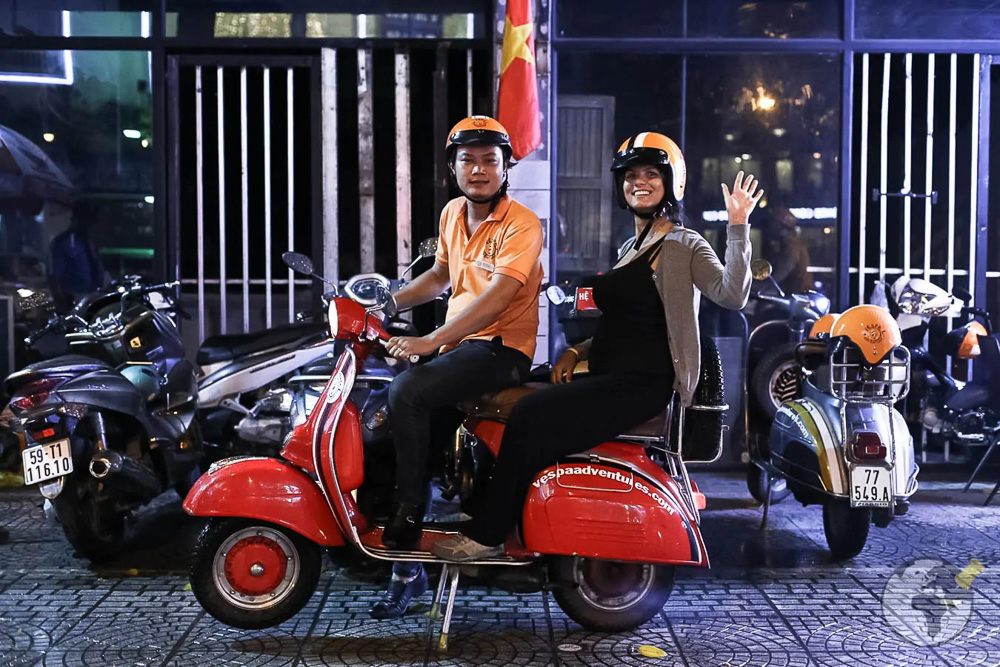 Mulher na garupa de scooter vermelha, à noite.