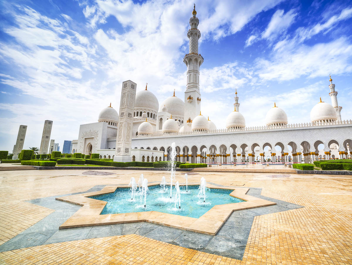 Cúpulas brancas e minarete da Grande Mesquita Sheikh Zayed, em Abu Dhabi, com fonte em formato de estrela no pátio.