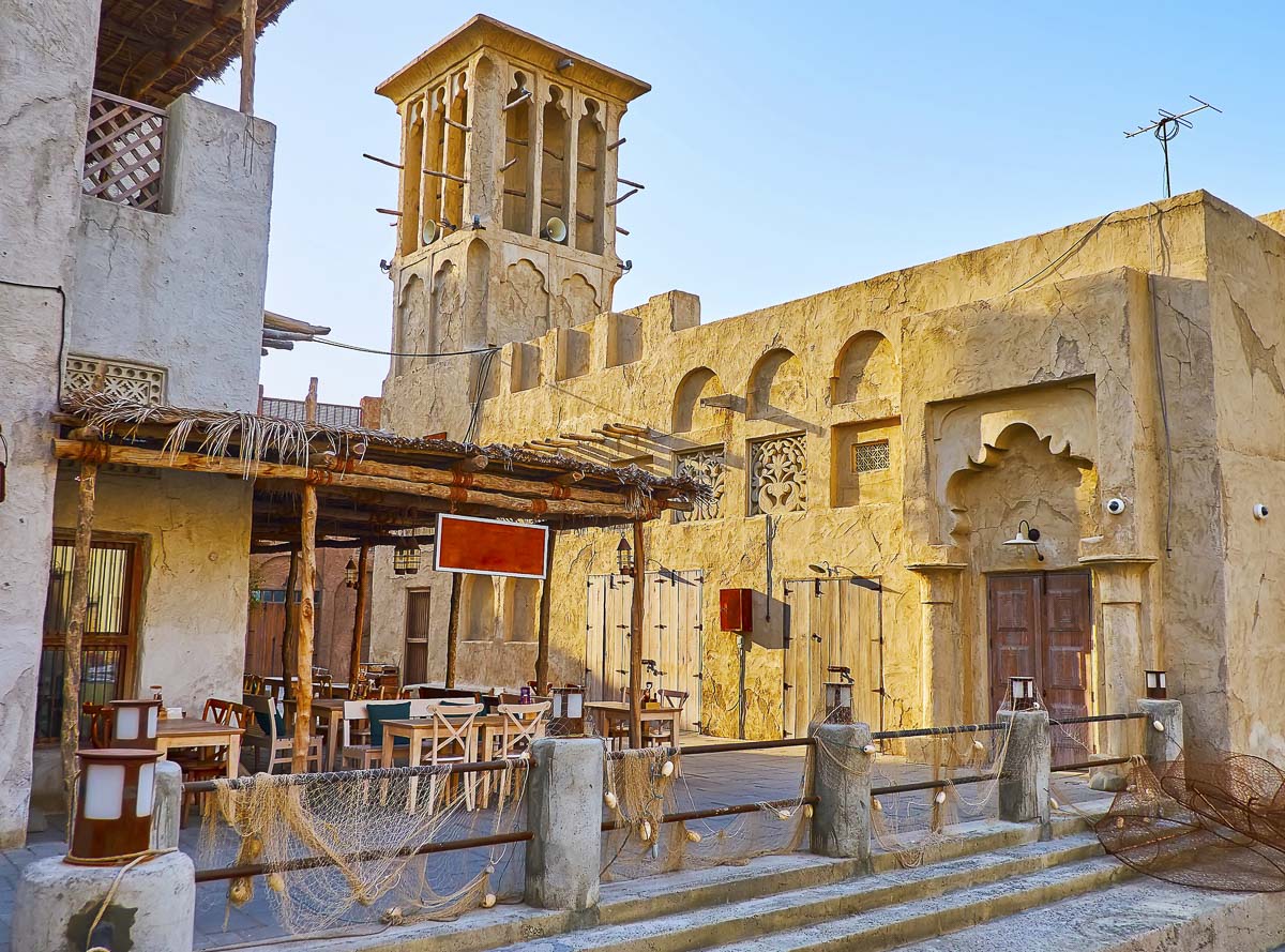 Construções de barro e torre de vento no bairro histórico Al Fahidi Al Bastakiya, em Dubai, com mesas ao ar livre.