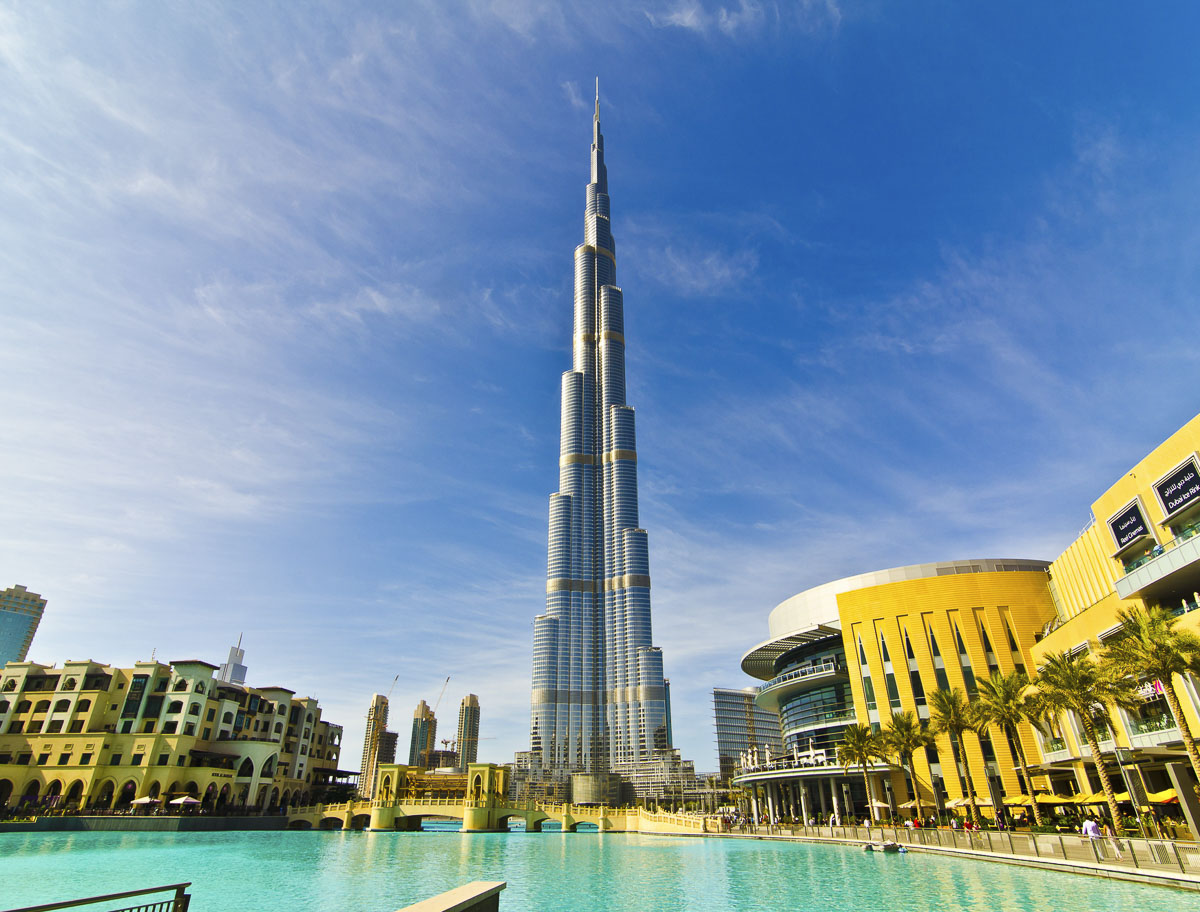 Burj Khalifa visto da área do Dubai Mall, com lago azul e prédios ao redor.