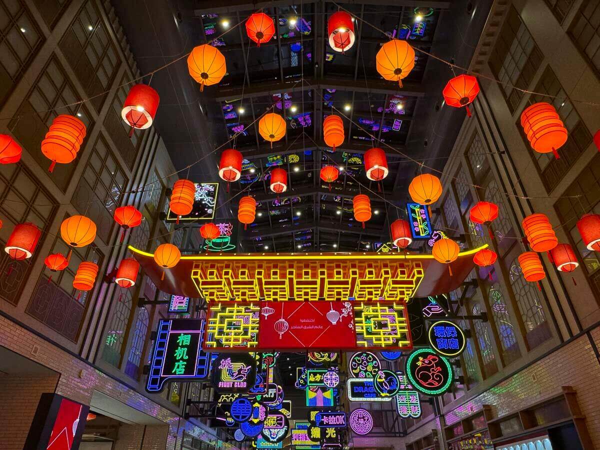 Área interna do Dubai Mall decorada com lanternas vermelhas e letreiros neon coloridos.