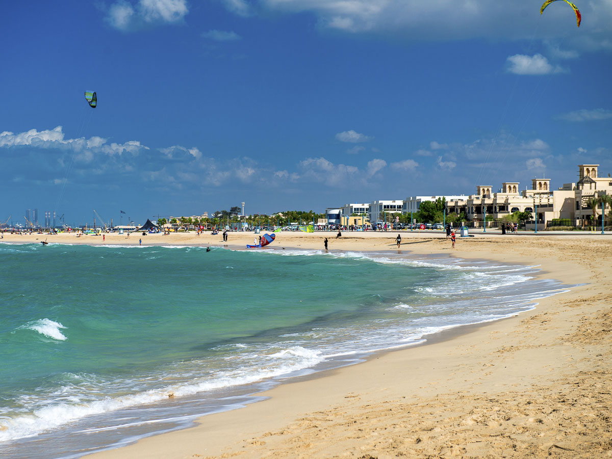 Kite Beach em Dubai com mar verde, areia clara e praticantes de kitesurf ao fundo.