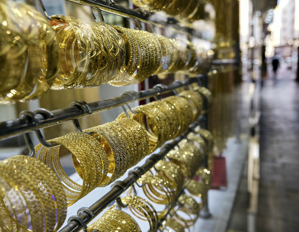 Pulseiras douradas em vitrine no Souk do Ouro, em Dubai, com corredor do mercado desfocado ao fundo.