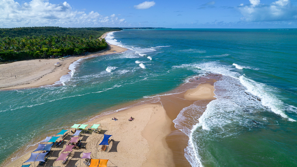 Praia da Barra em Caraíva vista de cima, com tendas coloridas na areia e o rio ao lado