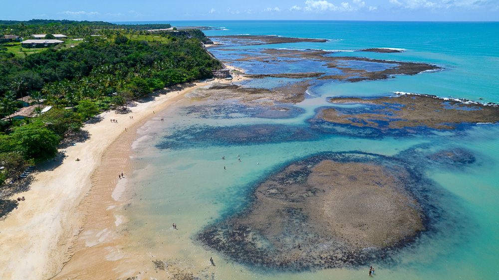 Praia do Espelho vista de cima, com piscinas naturais e mar em tons de azul e verde.