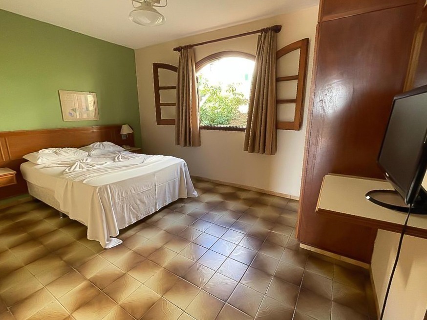 Quarto do Hotel Fazenda São Matheus em Serra Negra com cama de casal, janela com cortinas e móveis de madeira