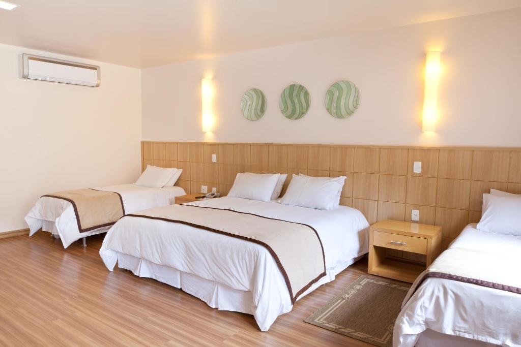 Quarto do Village Le Canton em Teresópolis com cama de casal, duas camas de solteiro e decoração em tons claros