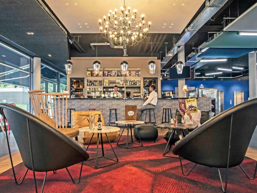 Área comum do ibis Styles Genève Carouge com bar, poltronas e iluminação moderna