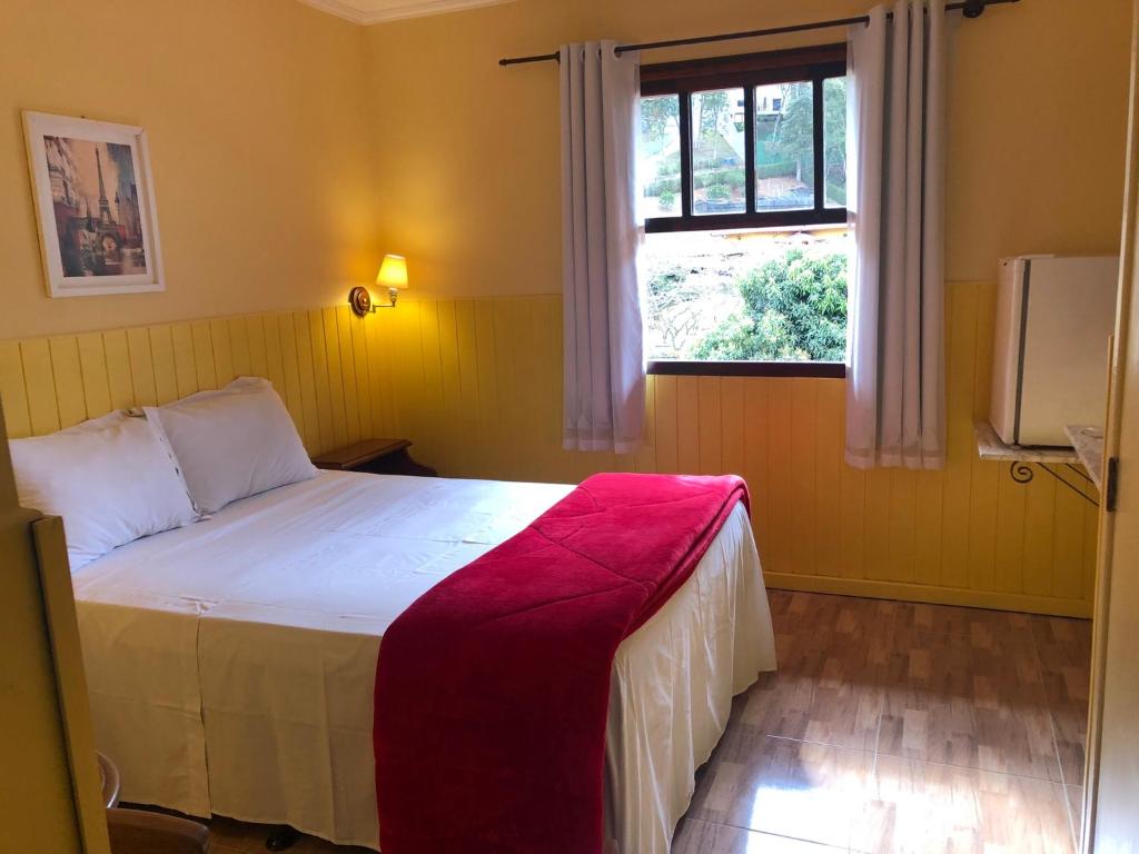 Quarto da Villa Mia Duo em Itaipava com cama de casal, parede amarela e janela com vista para área verde