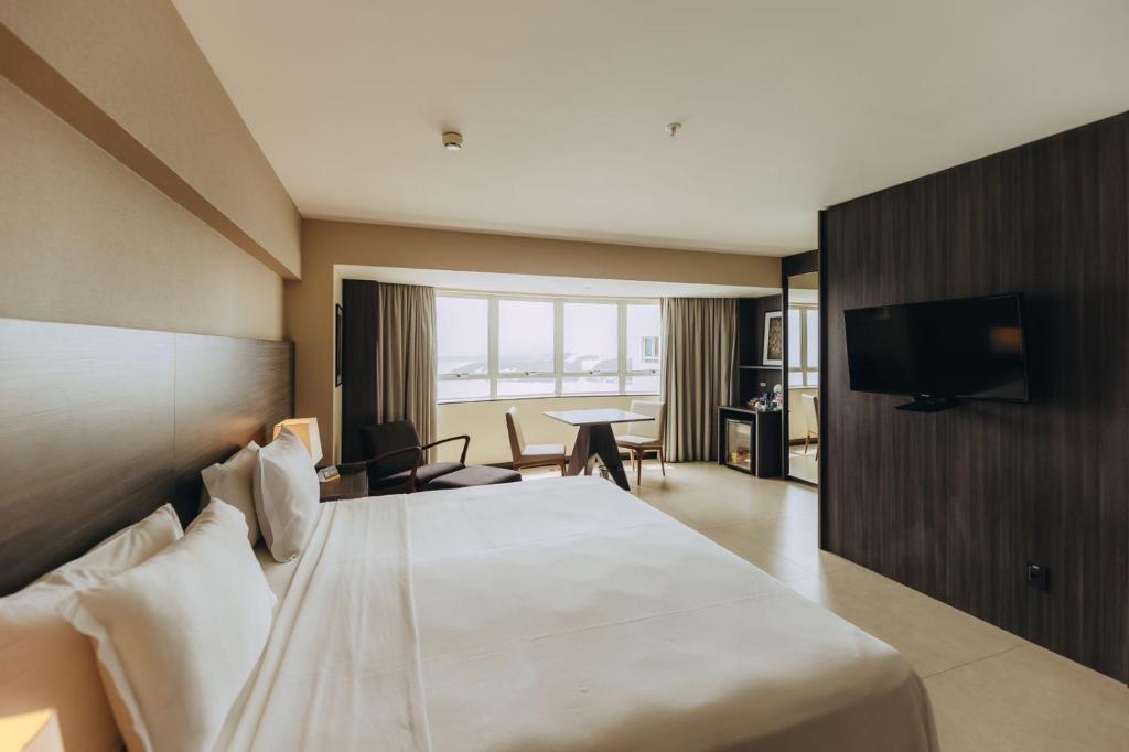 Quarto do Golden Tulip Natal Ponta Negra em Natal com cama de casal, TV na parede e mesa próxima à janela