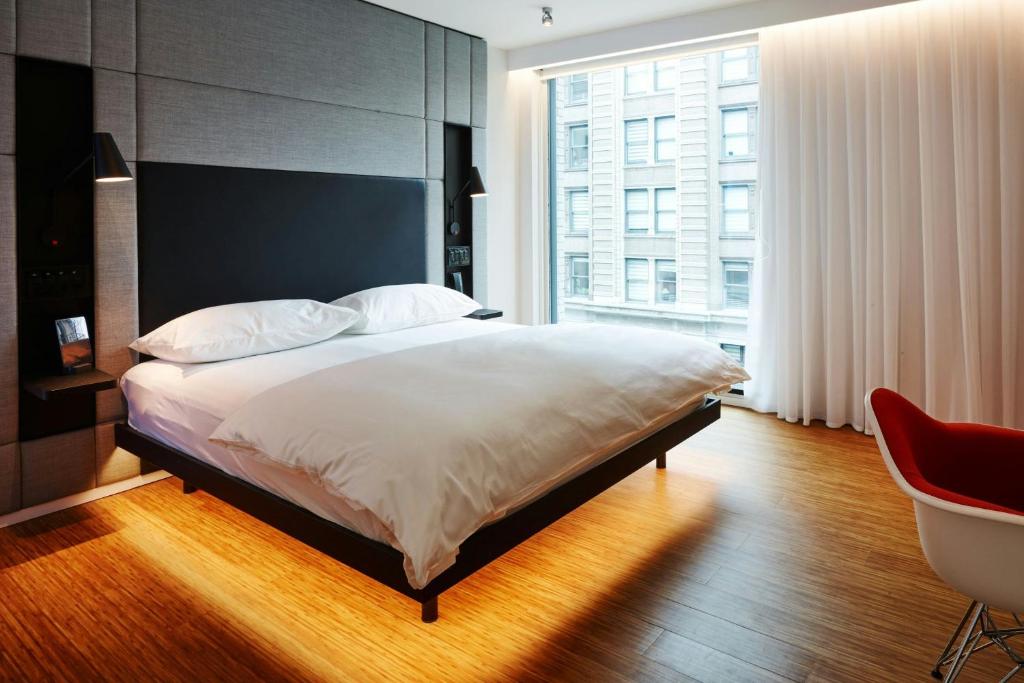 Quarto do citizenM Los Angeles Downtown com cama grande, janela ampla e cadeira vermelha