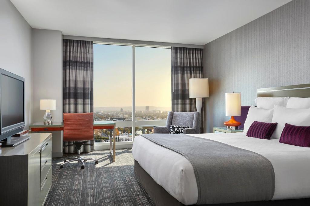Quarto do Loews Hollywood Hotel com cama de casal, mesa de trabalho e janela com vista para Los Angeles