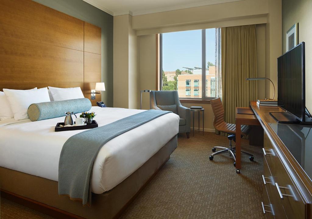 Quarto do Luskin Hotel com cama de casal, poltrona, escrivaninha e televisão