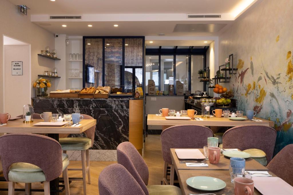Área de café da manhã do Hotel des Arts Montmartre, com mesas pequenas, cadeiras coloridas e balcão com pães e frutas