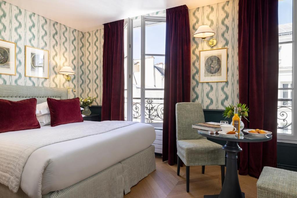 Quarto do Hotel du Champ de Mars, com cama branca, cortinas vinho e mesa redonda perto da janela