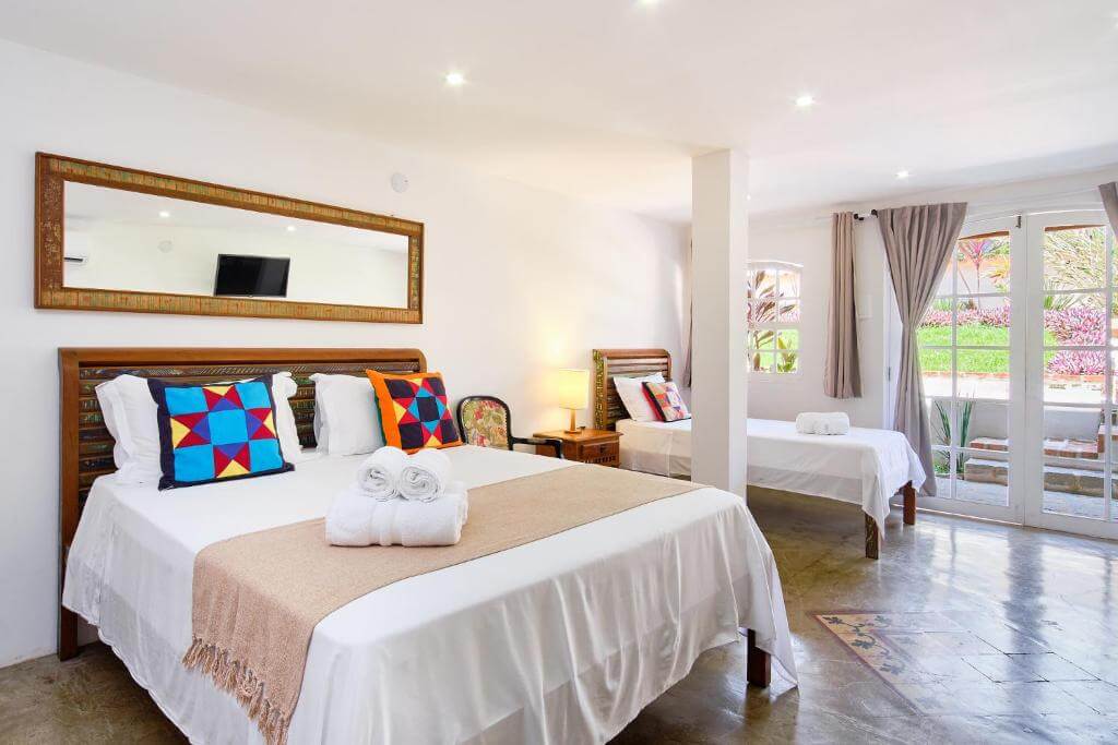 Quarto do Boutique Hotel Carpe Diem em Trindade com cama de casal e área integrada com cama de solteiro e portas de vidro