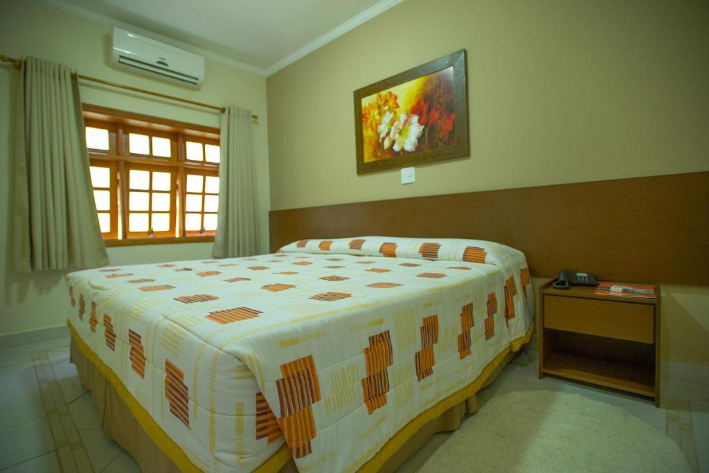 Quarto do Resort Fazenda São João em Águas de São Pedro com cama de casal, cabeceira de madeira e janela com cortinas