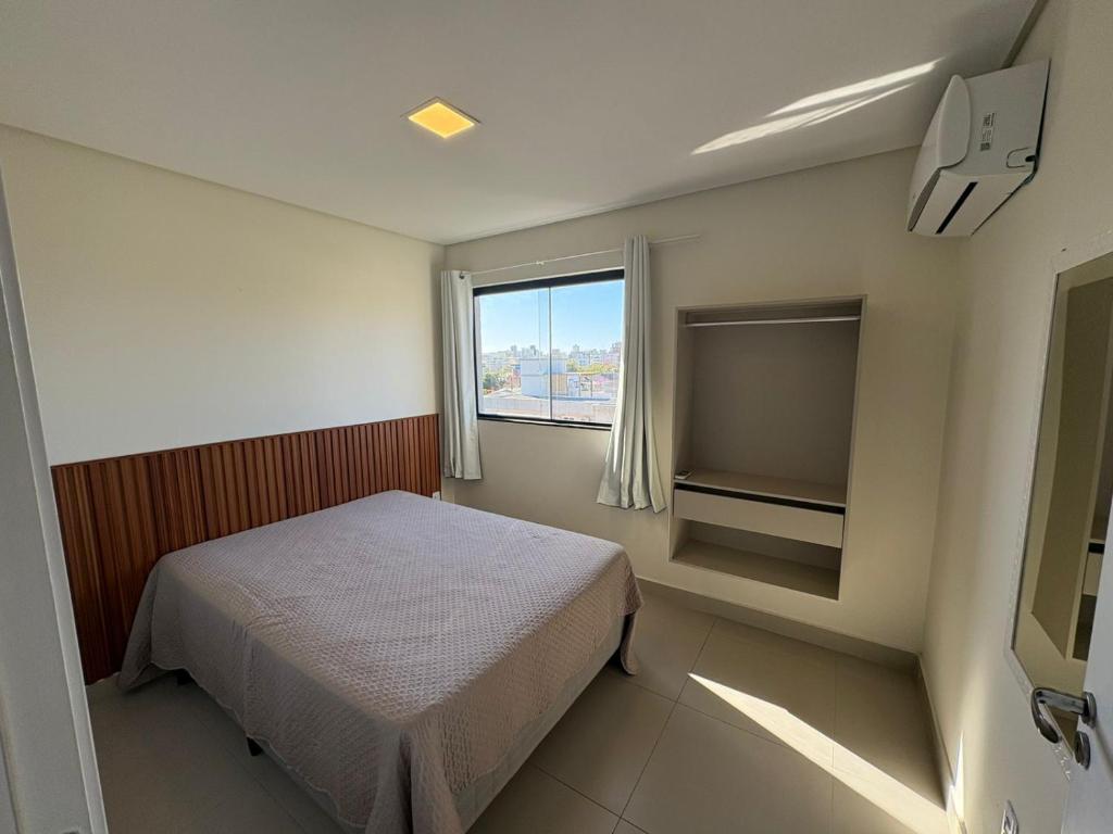 Quarto do Residencial Brisa do Mar em Bombinhas com cama de casal, janela e armário aberto