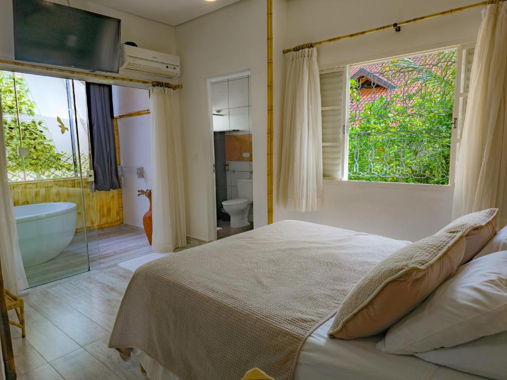Quarto do Hotel Natural Brotas com cama de casal, banheira integrada e janela com vista para área verde