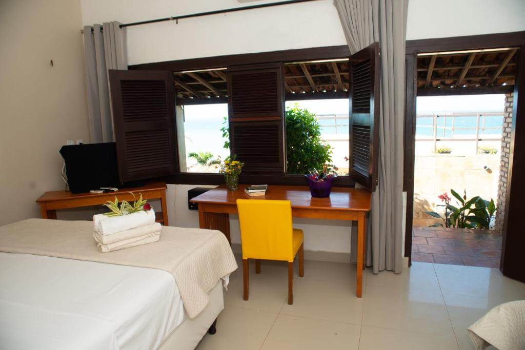 Quarto da Pousada Vila Canoa em Canoa Quebrada com cama de casal, mesa de madeira e vista para o mar