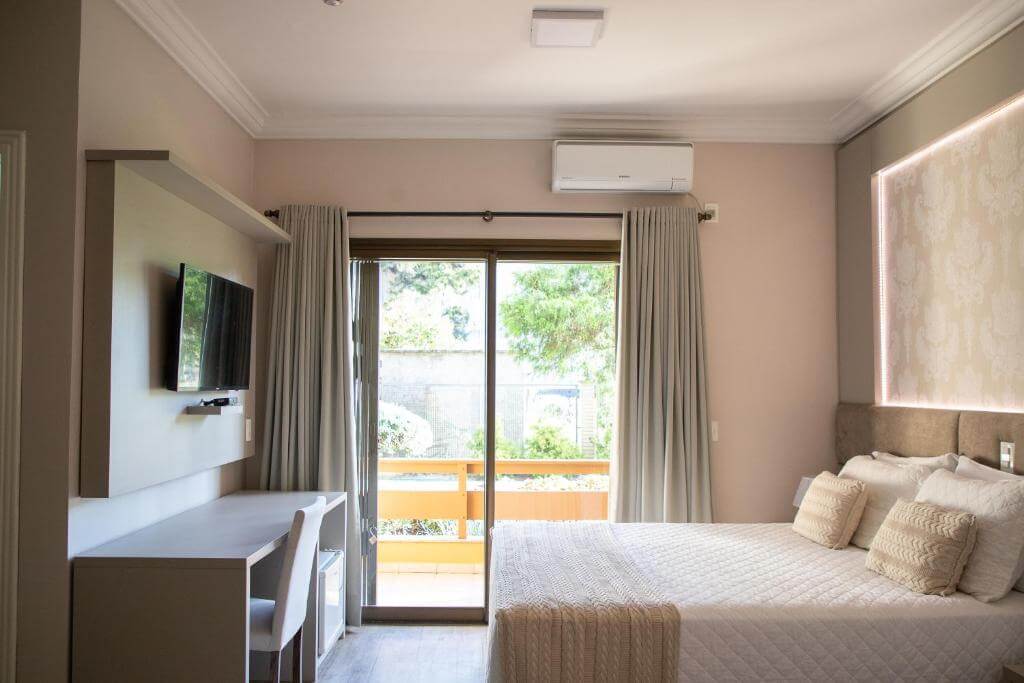 Quarto do Hotel Kaster com cama de casal, varanda e decoração em tons claros