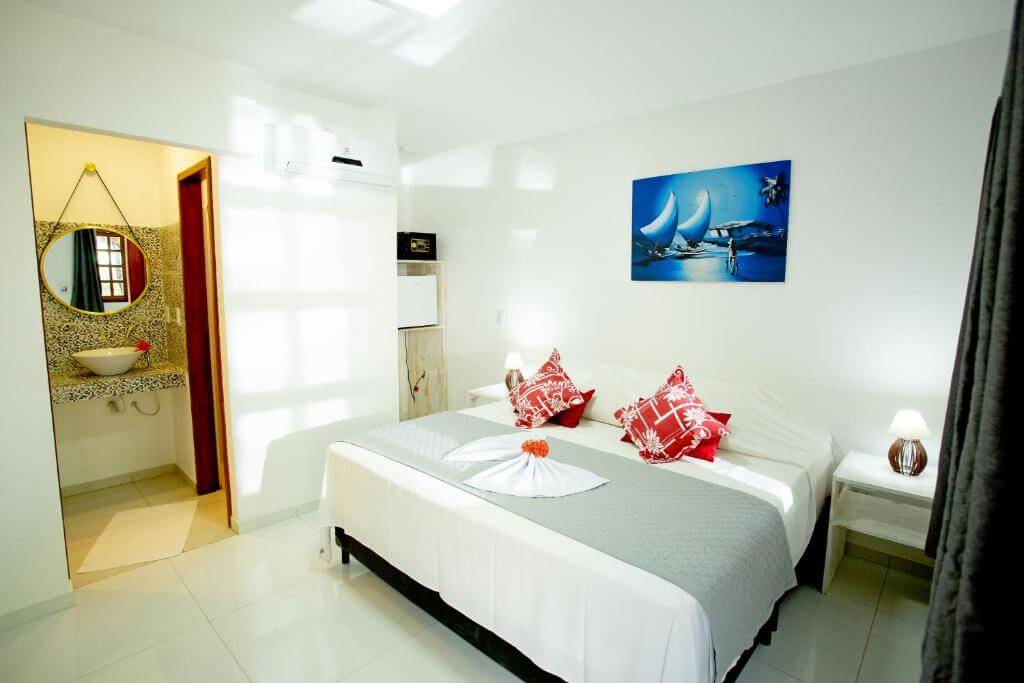 Quarto da Pousada Villa Caju com decoração branca e almofadas vermelhas