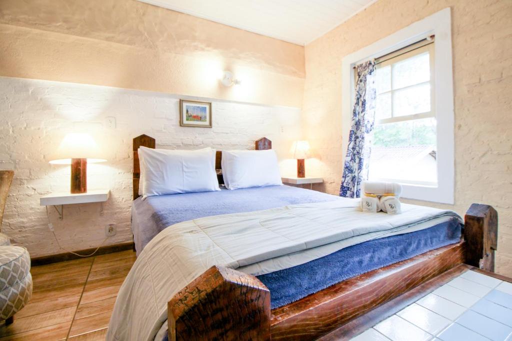 Quarto simples e aconchegante na Velinn Pousada Cesar em Santo Antônio do Pinhal, cama de madeira e janela com cortina
