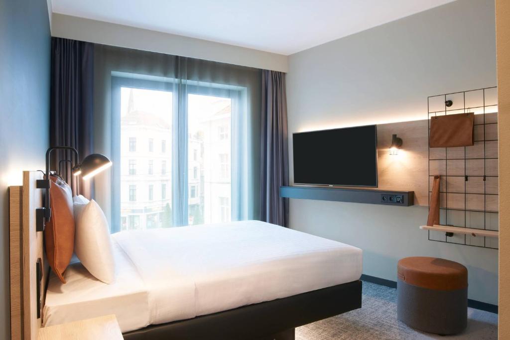 Quarto do Moxy Brussels City Center em Bruxelas com cama de casal, televisão e janela ampla.