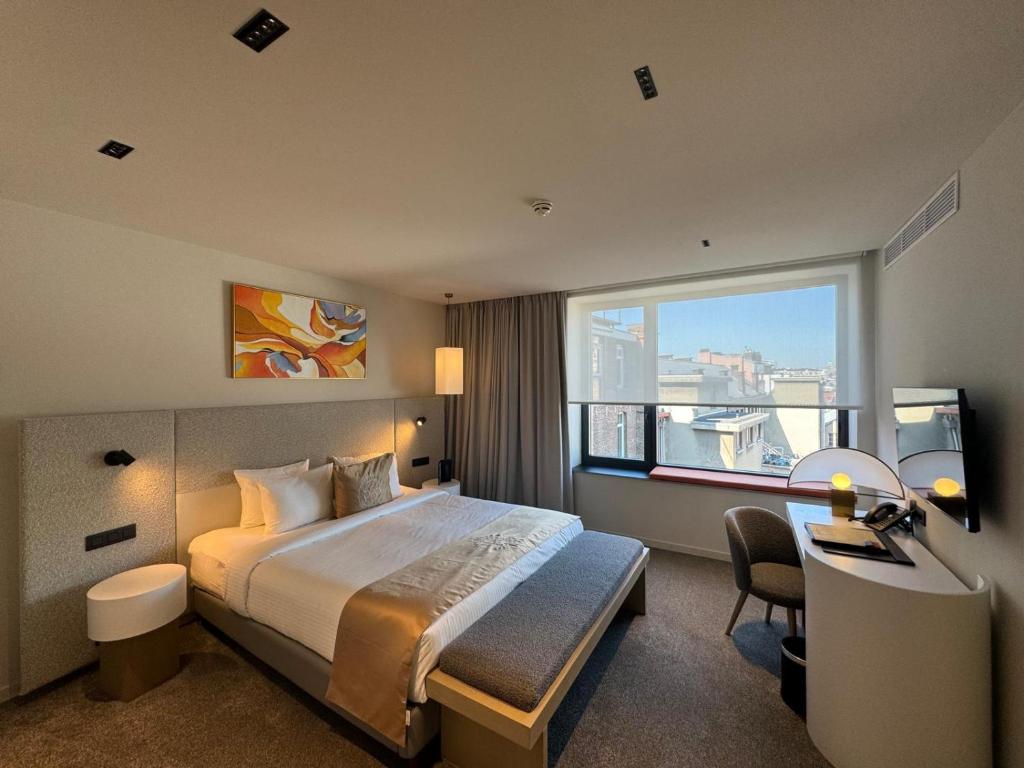 Quarto do OPO Hotel em Bruxelas com cama de casal, mesa de trabalho e vista urbana pela janela.