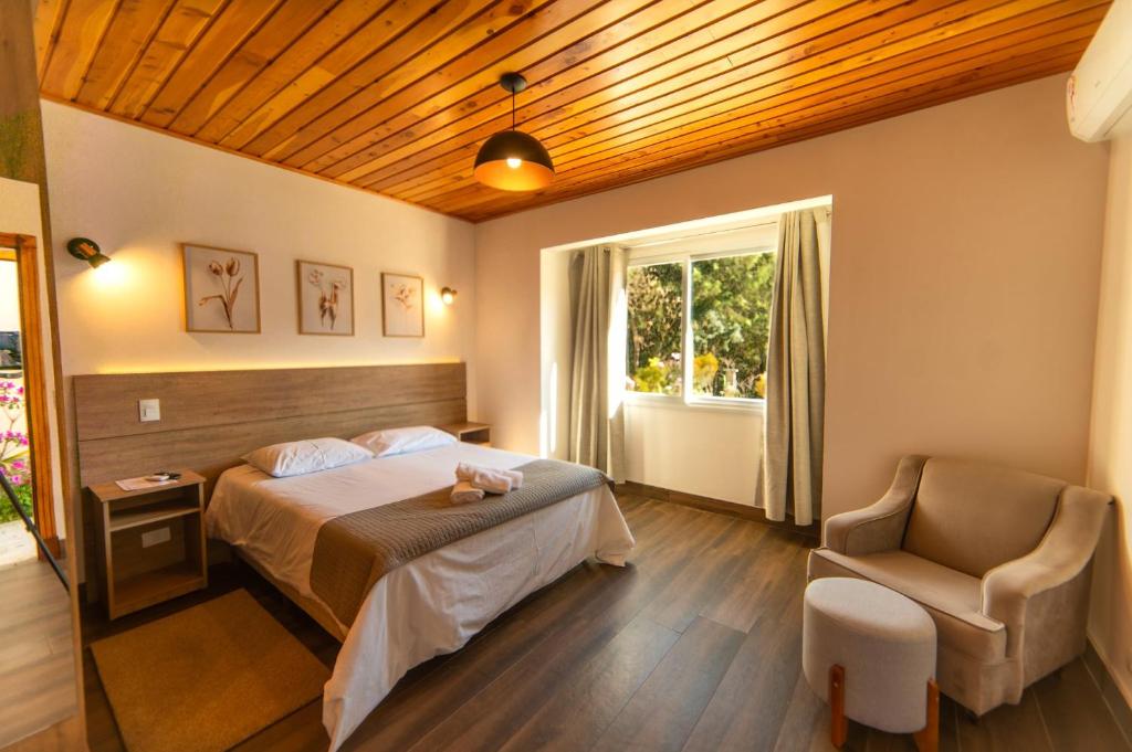 Quarto da Pousada Estilo de Campos em Campos do Jordão com cama de casal, poltrona e janela ampla.