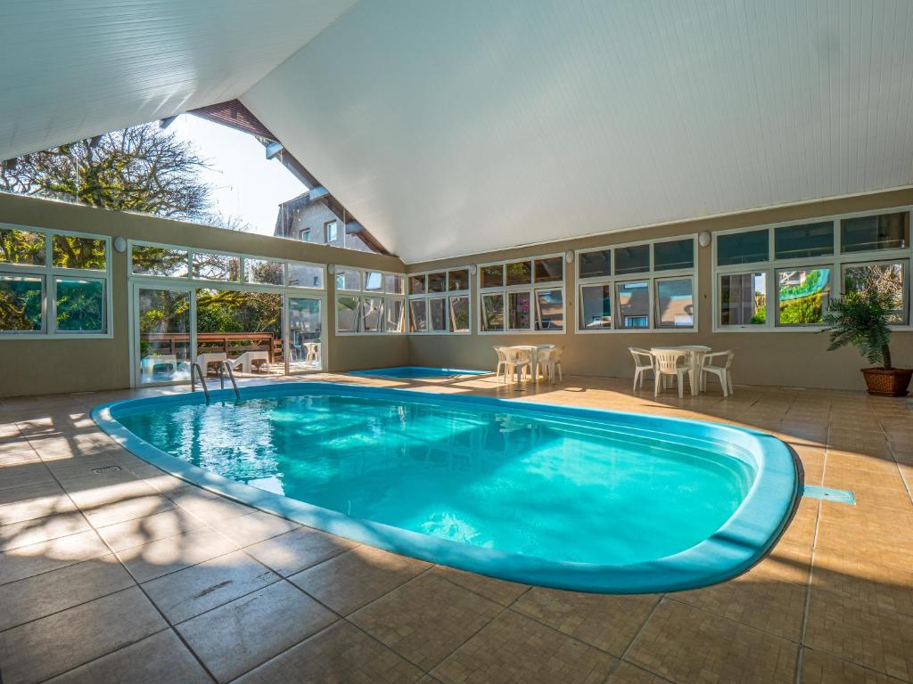 Piscina coberta do Hotel Fioreze Quero Quero, em Gramado, cercada por janelas e mesas com cadeiras brancas