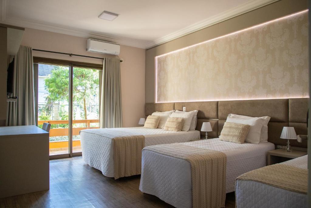Quarto do Hotel Kaster, em Gramado, com três camas, mantas bege e porta de vidro voltada para uma varanda