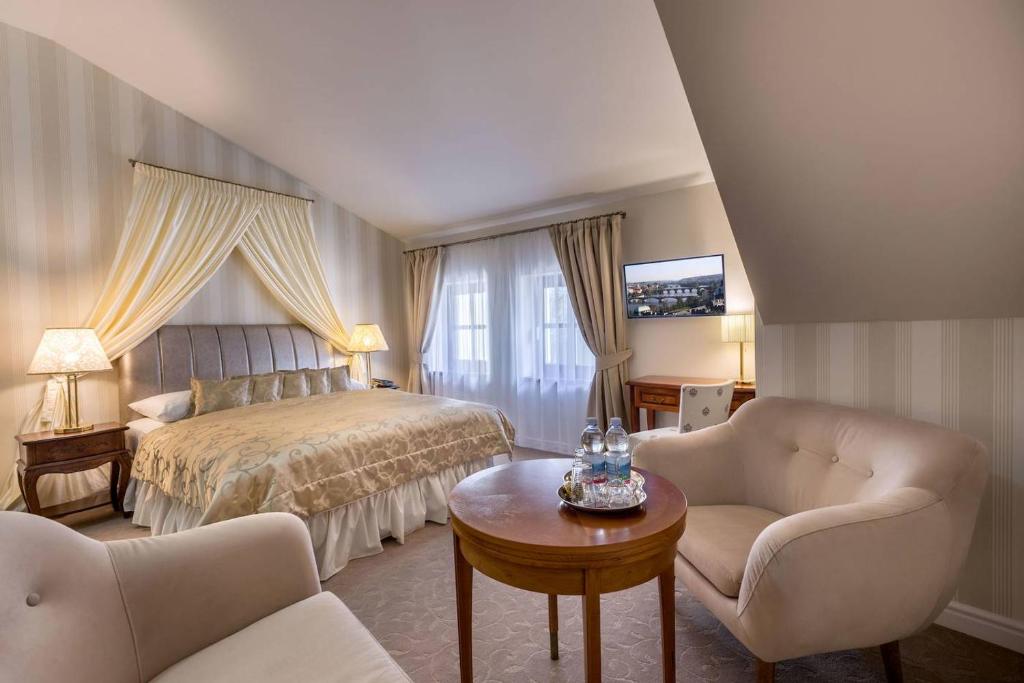 Quarto do Hotel Hoffmeister, em Praga, com cama de casal, poltronas claras e janela com cortinas bege